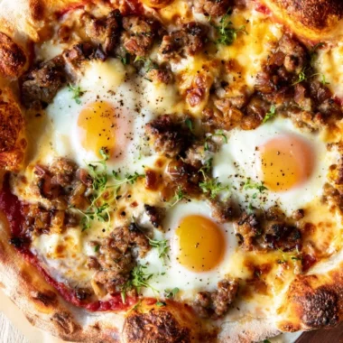 Sausage breakfast pizza topped with cheese and herbs on a wooden table