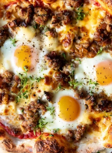 Sausage breakfast pizza topped with cheese and herbs on a wooden table