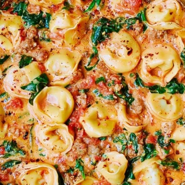 Creamy tortellini with sausage, spinach, tomatoes, and mozzarella served in a bowl.